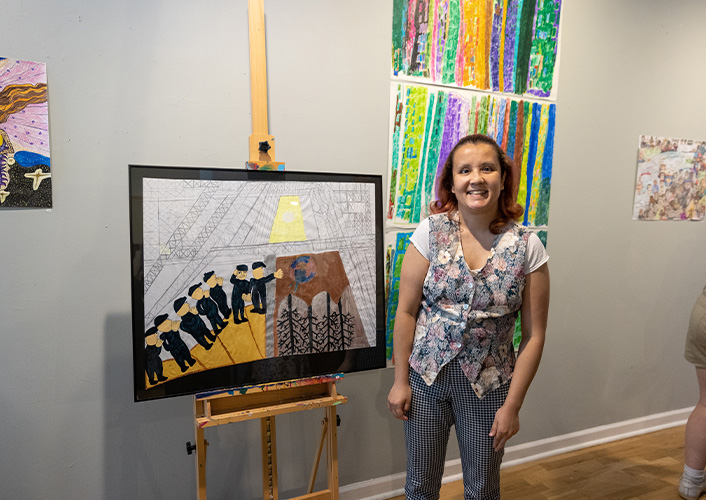 An MDAC artist smiling next to her painting on a canvas.