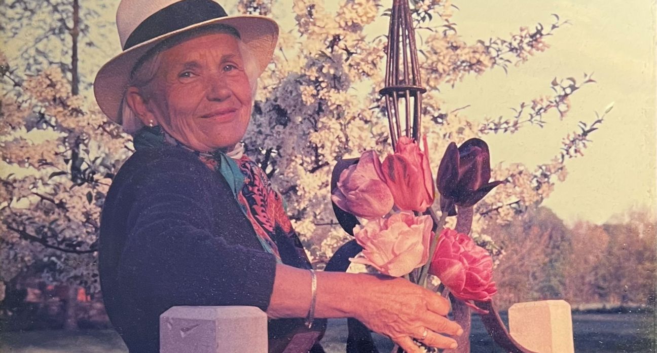 Maggie Daly wearing a hat and scarf while holding a bouquet of flowers outside.