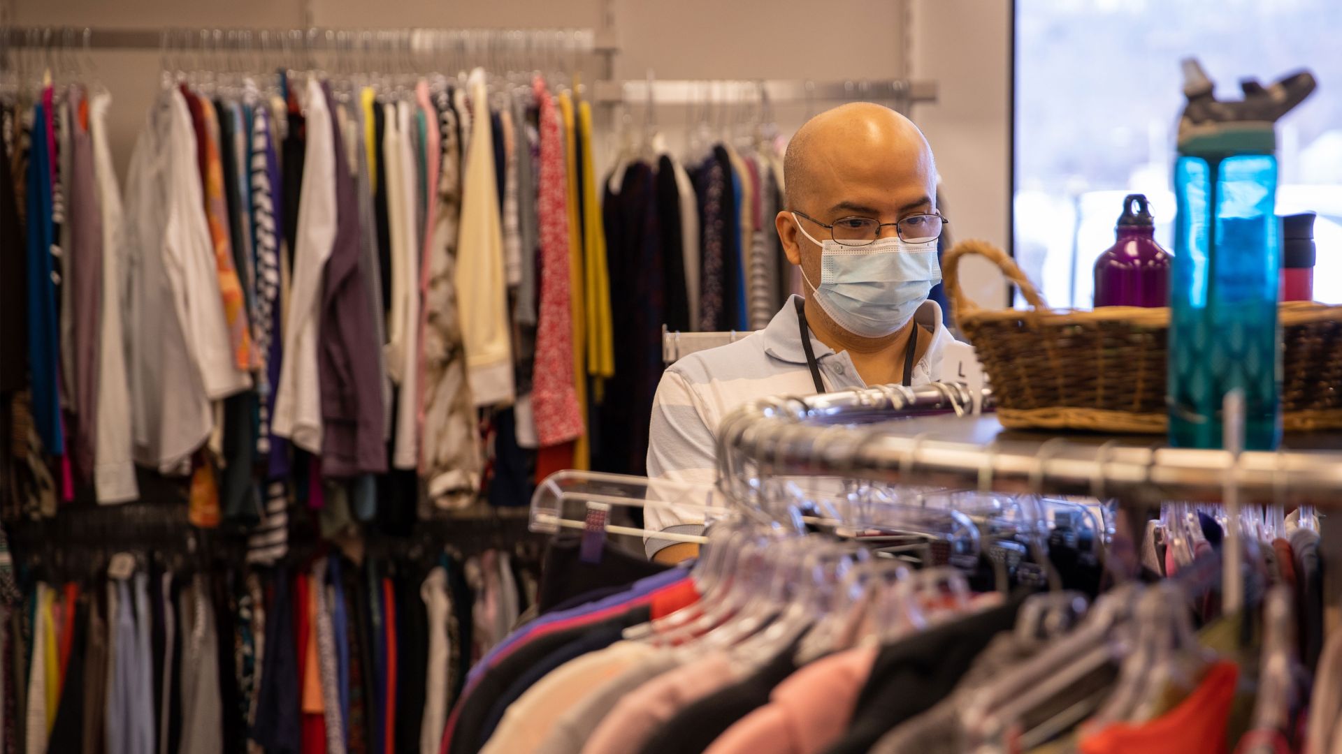 Person wearing glasses and a face mask looking through a clothing rack.