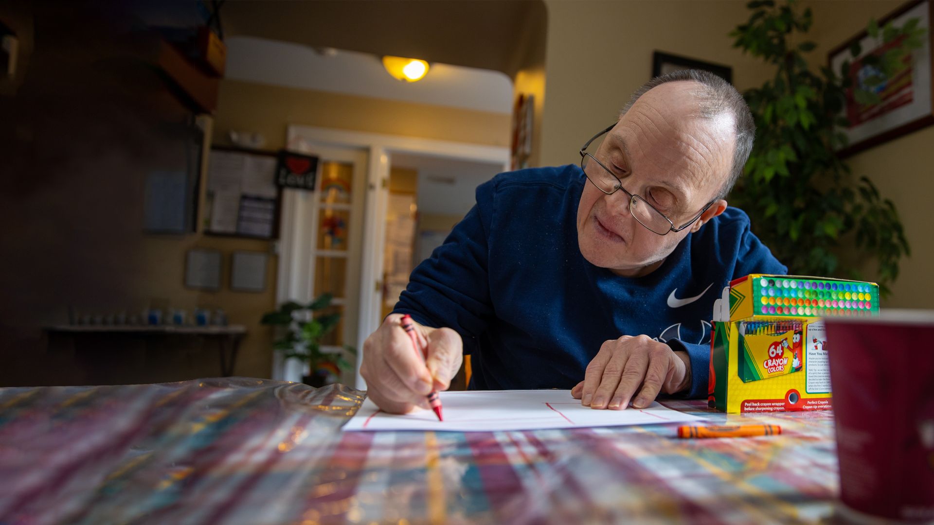 A man wearing glasses coloring on a sheet of paper in a group home.