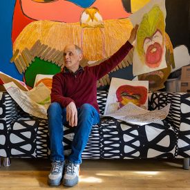 Man on black and white couch holding artwork in front of a colorful mural.