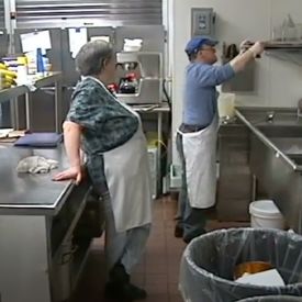 Two adults wearing aprons working together in a kitchen.