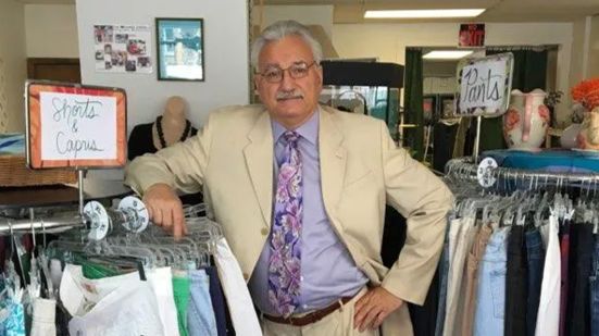 A man in a suit and tie leaning against a clothing rack.