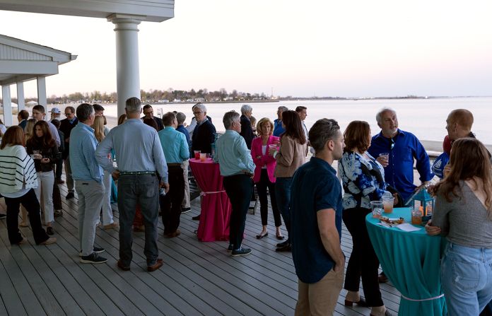 Group of people socializing on an outside patio by the water at a fundraising event.