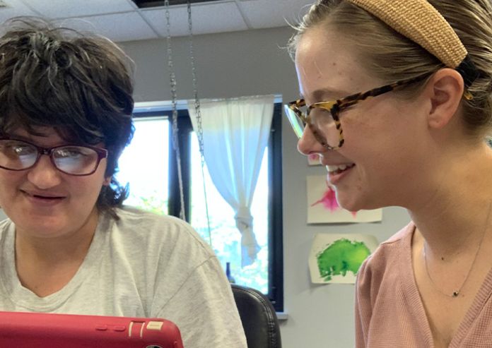 Two girls wearing glasses smiling looking at an iPad activity together.