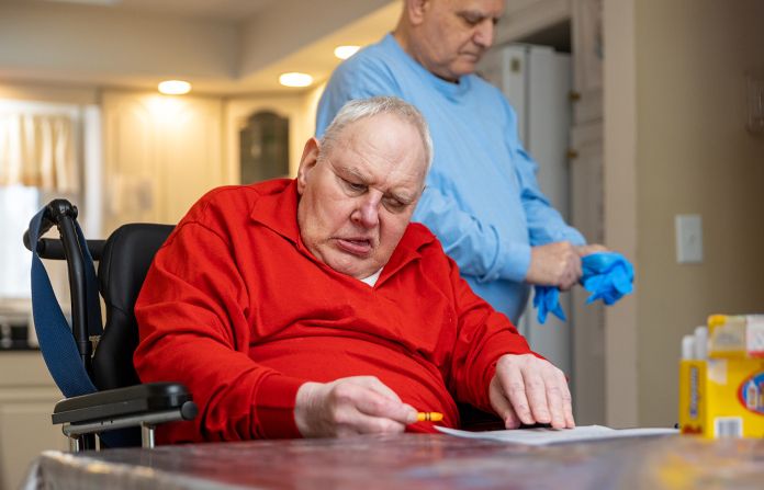 Man in wheelchair and red shirt coloring at a table.