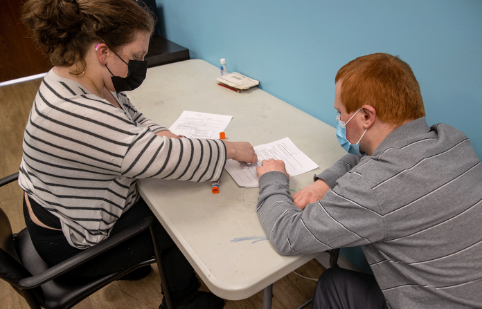 Woman in a striped shirt helping a young adult create a paper resume.
