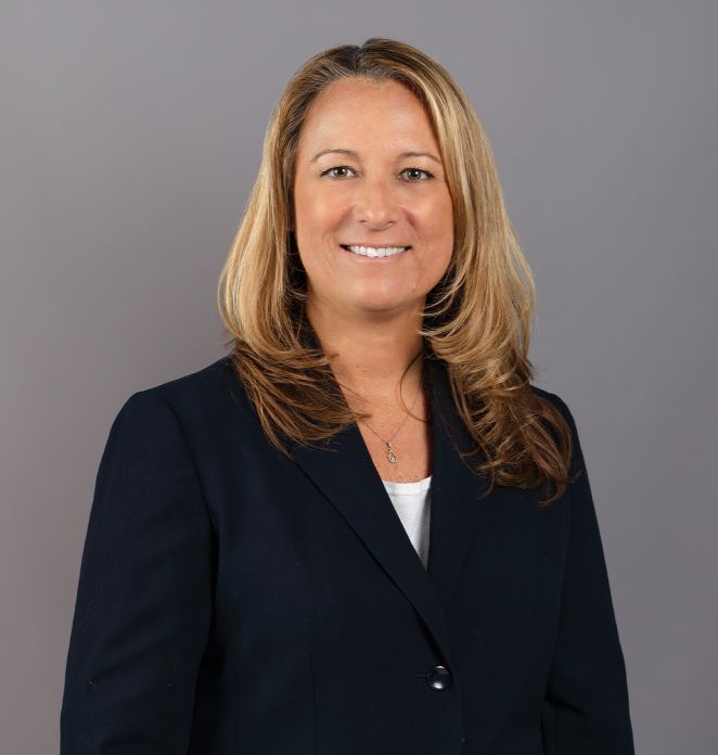 Valerie Rayher standing and smiling at the camera wearing a black blazer.